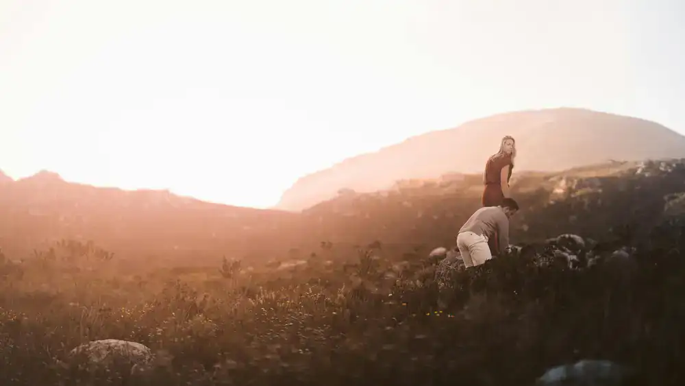 A couple walking through a sunlit field, showcasing an airy editorial photography style